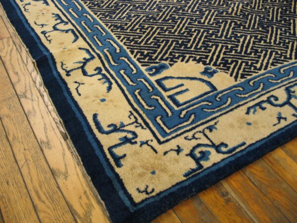 Tan and navy rug with geometric patterns and stylized borders rests on hardwood floors.