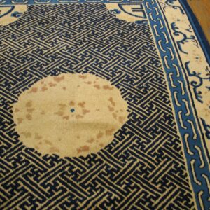 Navy and cream rug with a geometric pattern and borders rests on a glossy wooden floor.