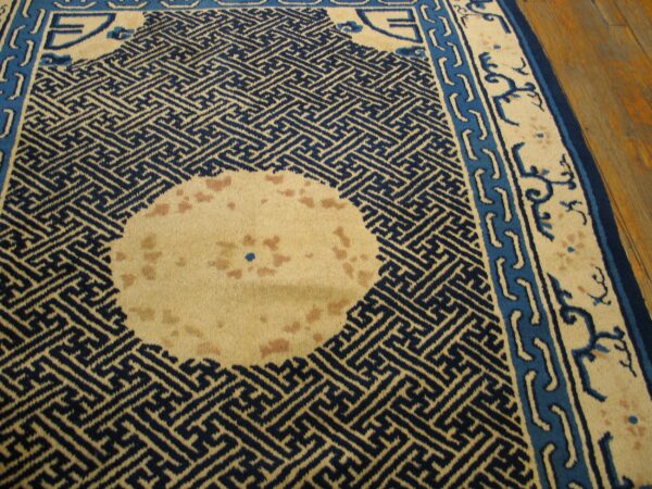 Navy and cream rug with a geometric pattern and borders rests on a glossy wooden floor.