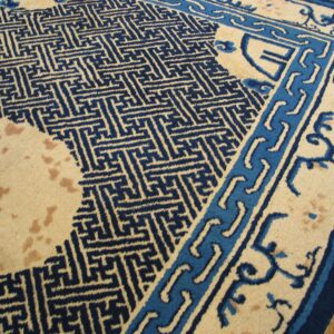 Beige rug with navy geometric fretwork and light blue borders rests on hardwood planks.