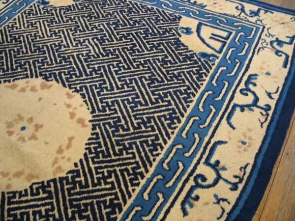 Beige rug with navy geometric fretwork and light blue borders rests on hardwood planks.