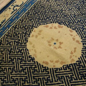 Navy and tan geometric rug featuring a spotted circular patch, bordered by light wood flooring.