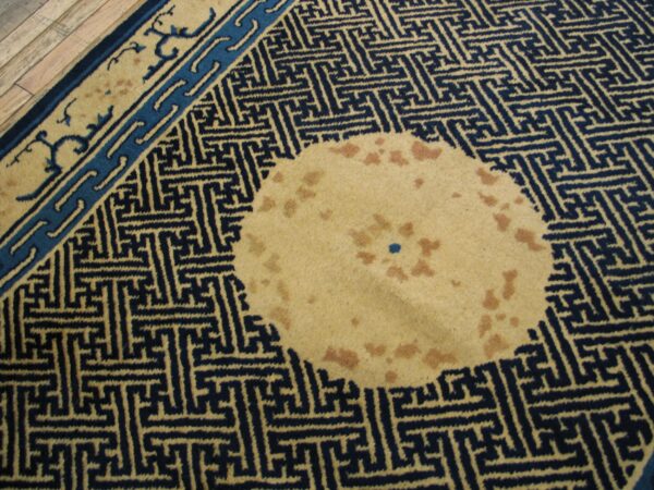 Navy and tan geometric rug featuring a spotted circular patch, bordered by light wood flooring.