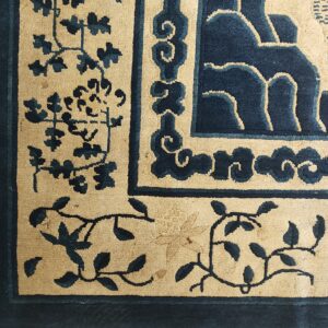 Navy blue and beige rug close-up detailing scroll borders and stylized floral vines.