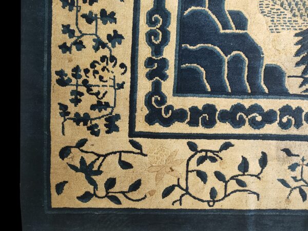 Navy blue and beige rug close-up detailing scroll borders and stylized floral vines.