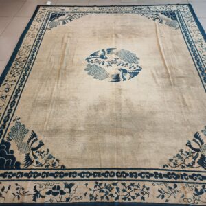 Cream and deep blue rug with a central bird motif and patterned borders, visible on a light tiled floor.