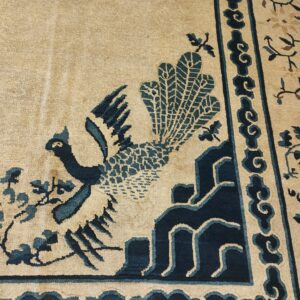 A low pile tan rug features a prominent indigo bird motif and matching ornamental border patterns.