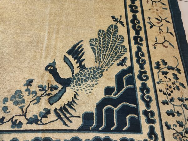 A low pile tan rug features a prominent indigo bird motif and matching ornamental border patterns.