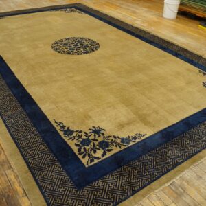 Large mustard and navy rug featuring a floral medallion and geometric fretwork border on wood floor.