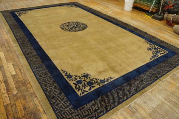 Large mustard and navy rug featuring a floral medallion and geometric fretwork border on wood floor.