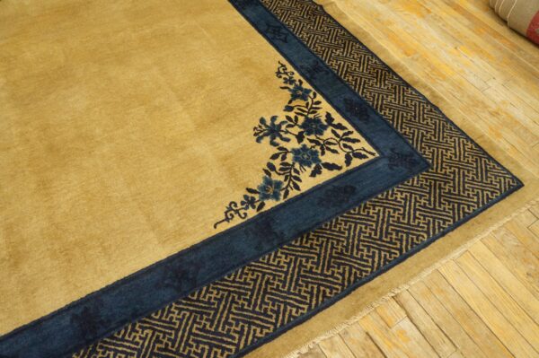 Golden rug featuring deep blue floral corner designs and a geometric fret border on light wood plank flooring.