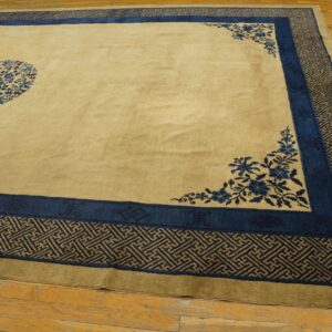 Tan rug with a blue floral medallion and wide, complex geometric borders resting on wood plank flooring.
