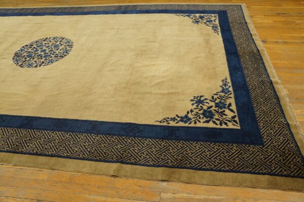Tan rug with a blue floral medallion and wide, complex geometric borders resting on wood plank flooring.