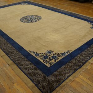 Tan rug with dark blue floral and key pattern borders displayed over distressed hardwood floors.