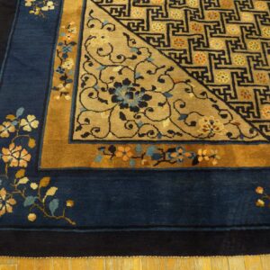 Close view of a blue and gold rug showing floral borders and a geometric field design on wood floor.