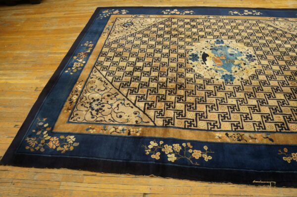 Low-pile rug in tan and deep blue featuring a complex repeating geometric and floral border design on wood floors.