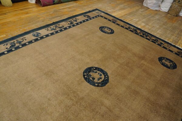 Camel field rug with elaborate dark blue borders and medallions covers light brown distressed wood flooring.