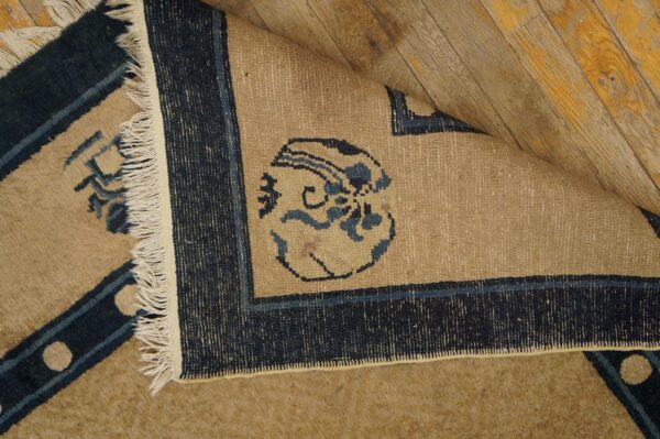 Beige and blue patterned rug corner folded back, revealing woven reverse side on yellow wood planks.