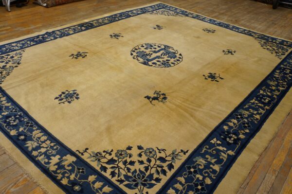 Square gold and blue rug featuring a central bird medallion and wide floral borders on distressed wood floors.