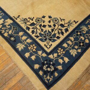 Close-up shows a tan rug corner with a blue floral border resting on diagonal wood planks.