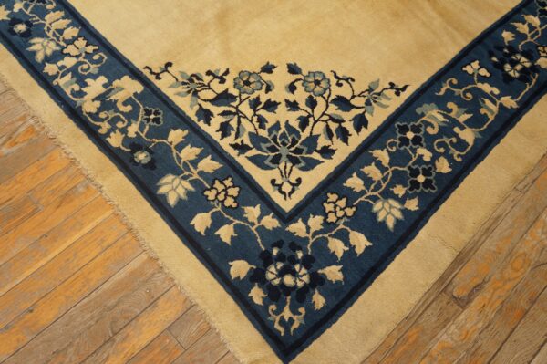 Close-up shows a tan rug corner with a blue floral border resting on diagonal wood planks.