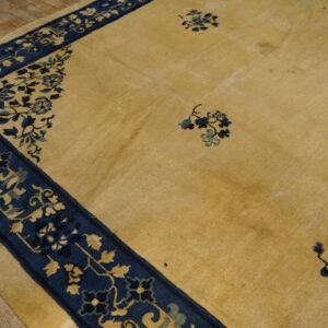 Yellow rug featuring a wide blue border and scattered floral accents on worn wood planks.