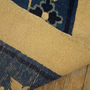 A blue and tan patterned rug is folded back to reveal its tightly woven backing on wood floors.