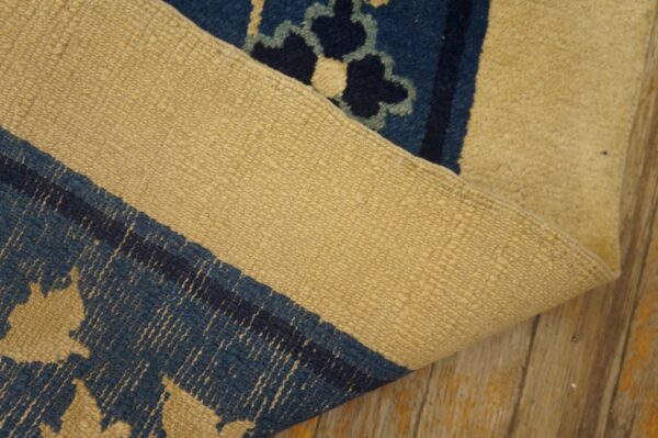A blue and tan patterned rug is folded back to reveal its tightly woven backing on wood floors.