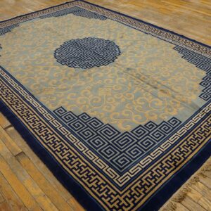 Pale blue rug with a beige repeating scroll pattern and navy geometric borders on wooden flooring.