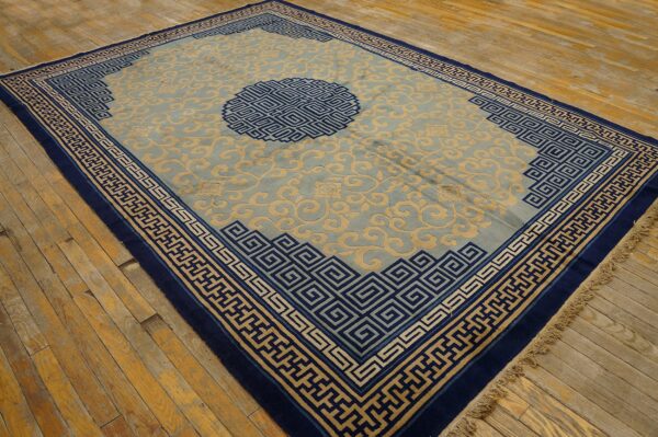 Pale blue rug with a beige repeating scroll pattern and navy geometric borders on wooden flooring.