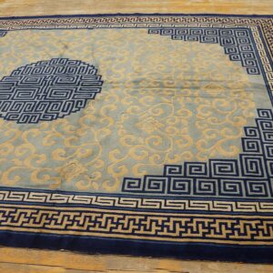 Light blue rug with tan floral scrolls, deep blue Greek key borders, and a medallion on wood planks.
