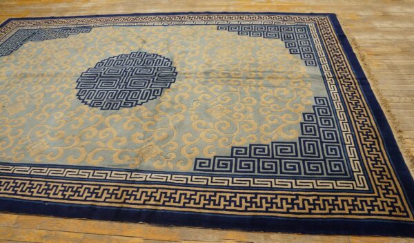 Light blue rug with tan floral scrolls, deep blue greek key borders, and a medallion on wood planks.
