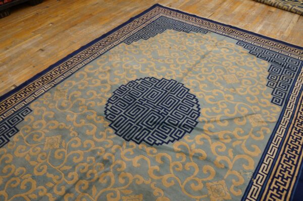 Pale blue rug with tan scrolling patterns and navy geometric borders laid on wood flooring.