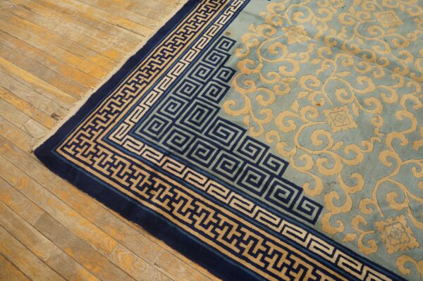 Teal rug with carved tan scrolling motifs and navy geometric borders shown on rustic wood flooring.
