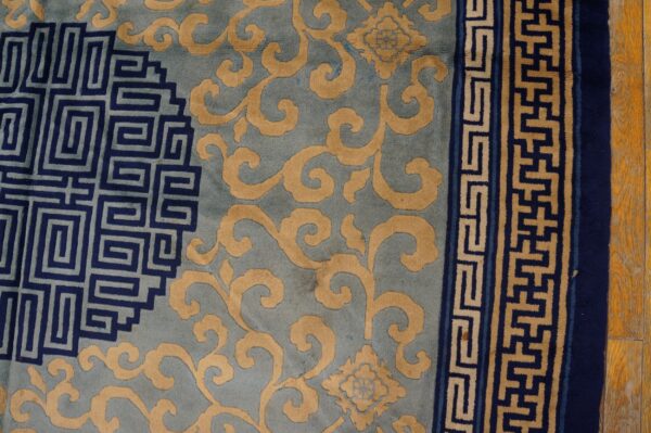 Close-up of a rug with blue, gold, and navy patterns, featuring scrolls and geometric borders on a wood floor.