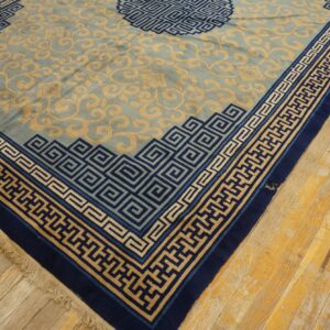 A large sage rug with tan scrollwork and intricate navy blue meander borders rests on worn wood flooring.