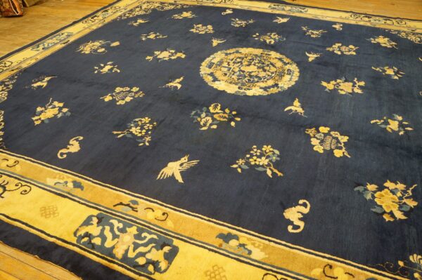 Deep blue rug with gold floral and bird motifs, a central medallion, and wide border on wood flooring.