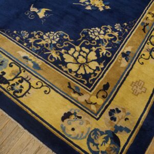 Detail of a deep blue rug with wide gold floral borders on light brown hardwood flooring.