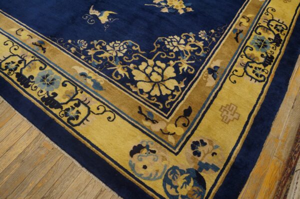 Detail of a deep blue rug with wide gold floral borders on light brown hardwood flooring.