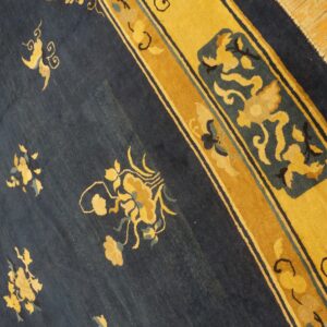 Diagonal view of a low-pile navy rug with scattered gold floral motifs and a wide yellow border on wood planks.