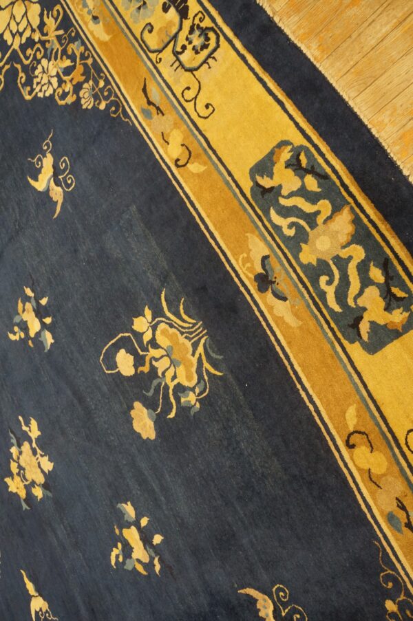 Diagonal view of a low-pile navy rug with scattered gold floral motifs and a wide yellow border on wood planks.