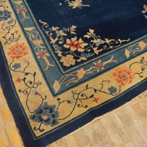 Floral patterned navy and tan rug with coral accents lying on worn wooden planks.