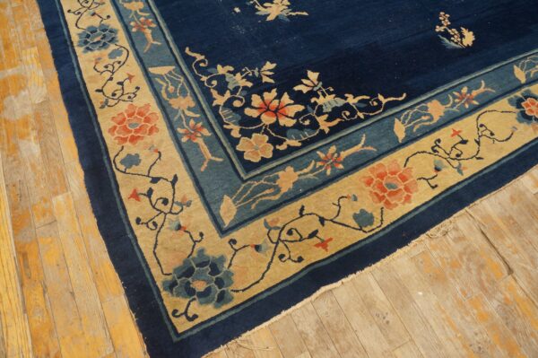 Floral patterned navy and tan rug with coral accents lying on worn wooden planks.