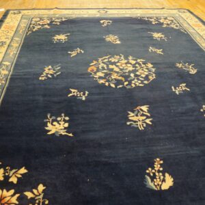 Deep blue rug with a wide cream border features scattered floral patterns on distressed wooden floors.