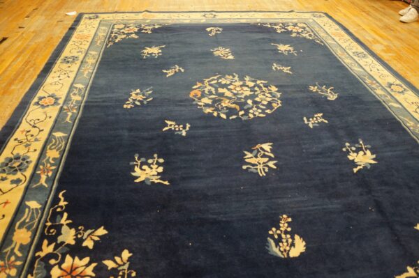 Deep blue rug with a wide cream border features scattered floral patterns on distressed wooden floors.