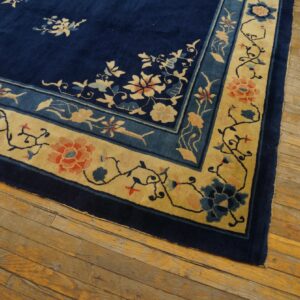 Navy blue rug with a light gold and blue floral pattern border on rustic hardwood floorboards.