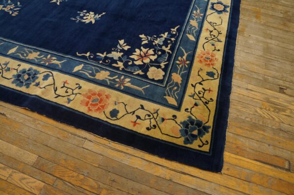 Navy blue rug with a light gold and blue floral pattern border on rustic hardwood floorboards.