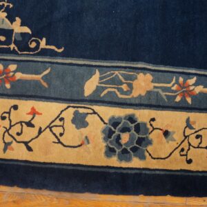 Navy blue rug border featuring wide tan and narrow blue stripes with intricate stylized floral motifs on wood flooring.