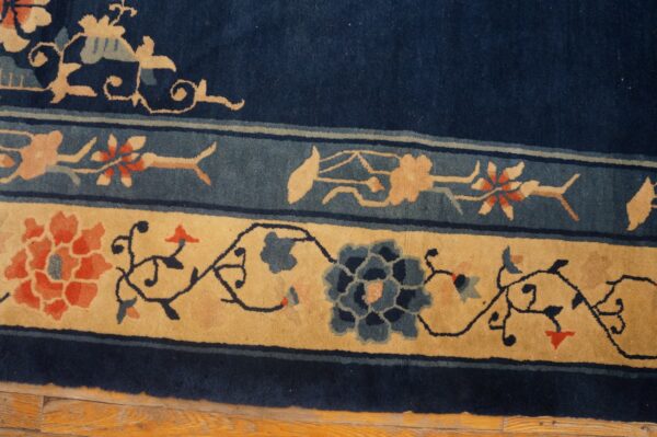 Navy blue rug border featuring wide tan and narrow blue stripes with intricate stylized floral motifs on wood flooring.