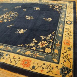 Navy blue floral rug featuring a wide golden yellow border with coral and teal accents on wooden floors.
